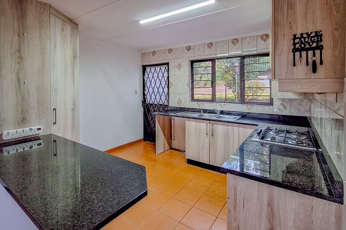 Functional kitchen featuring wood-look cabinetry, granite countertops, a built-in gas hob, and a security gate leading to the exterior.