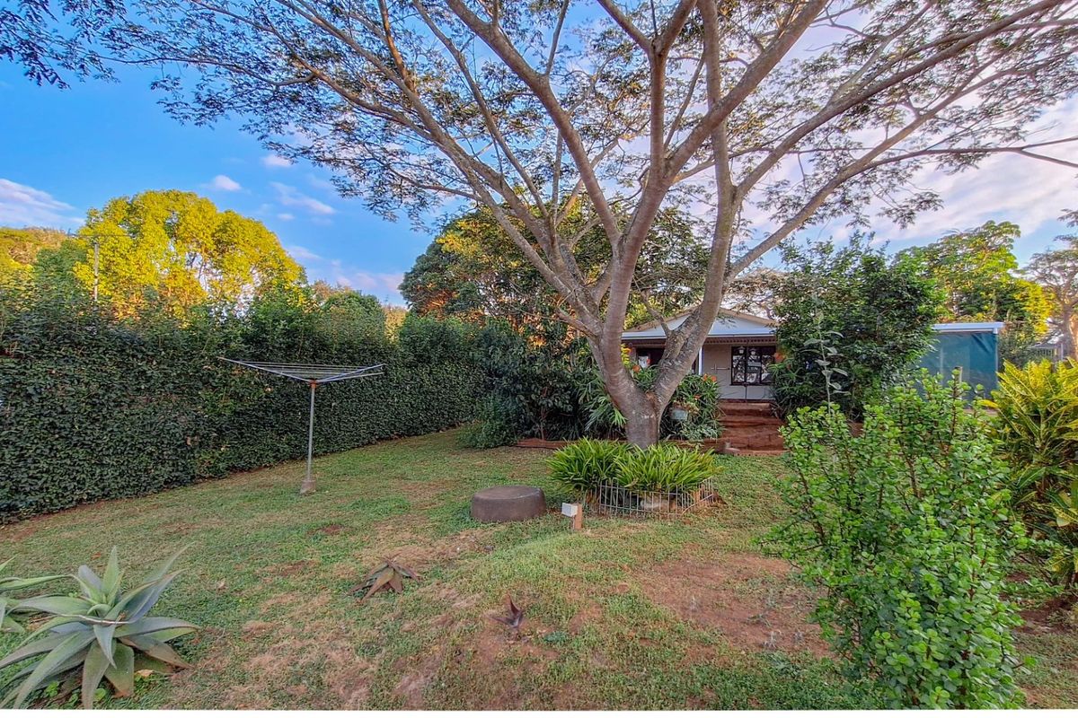 A view of the rear garden featuring established trees, manicured hedges, and a lawn area leading towards the cottage exterior.