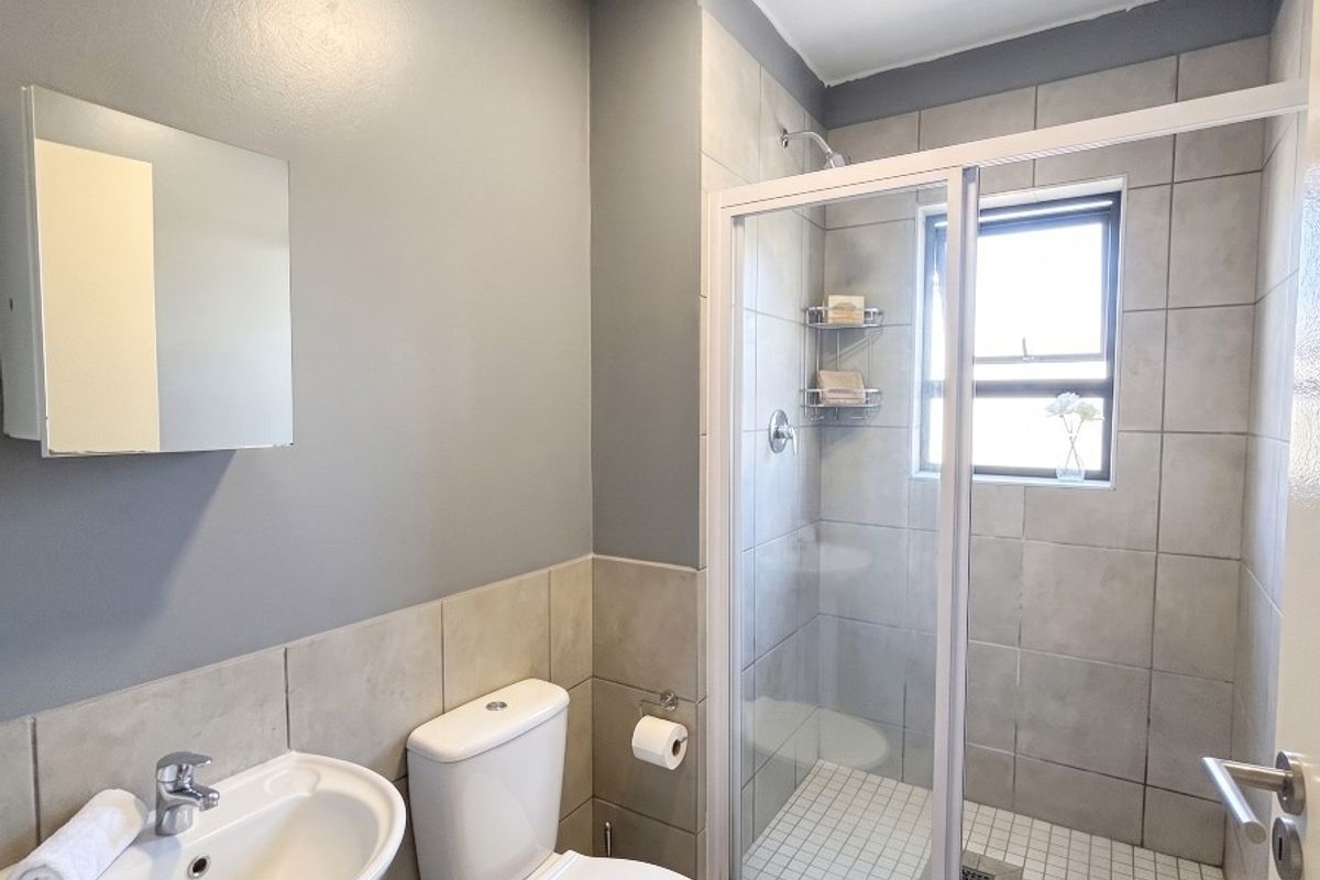 A clean and functional bathroom featuring a pedestal basin, toilet, and a glass-enclosed shower with neutral wall and floor tiling.