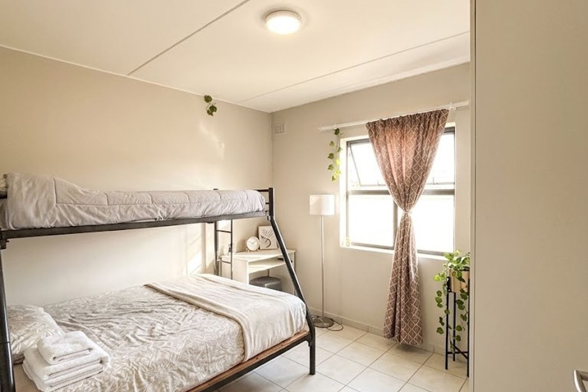 A functional bedroom featuring tiled flooring, a built-in cupboard, and a top-hung window providing natural light.