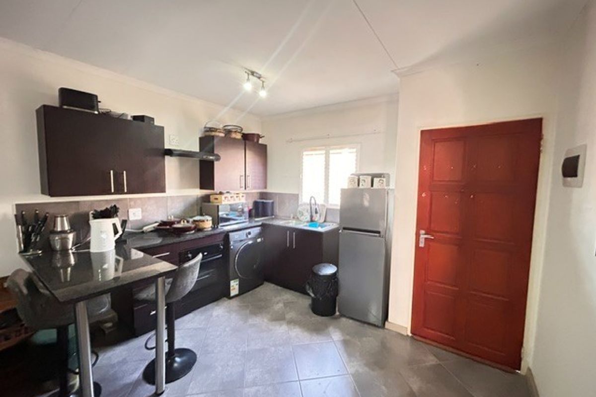 Compact kitchen featuring dark cabinetry, granite-look countertops, tiled flooring, and an integrated breakfast bar area with direct access to an exterior door.