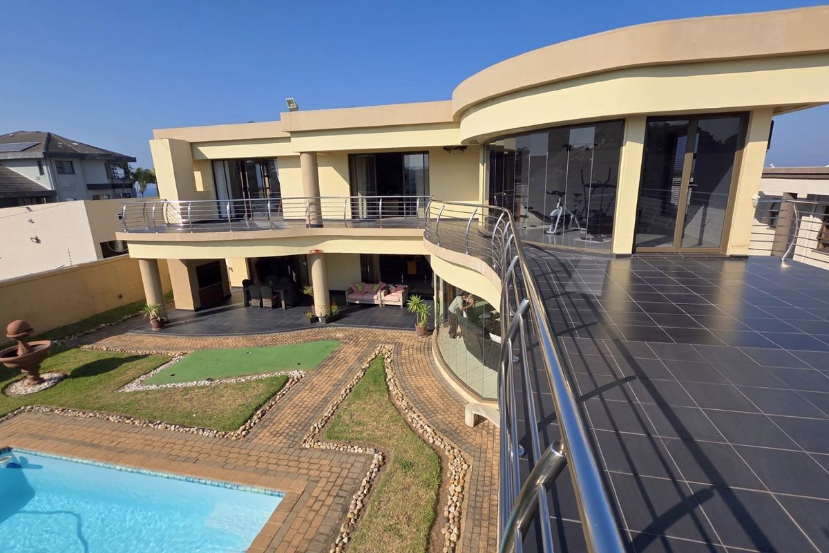 A spacious rear exterior view featuring a large balcony with stainless steel railings, a swimming pool, and landscaped garden areas.