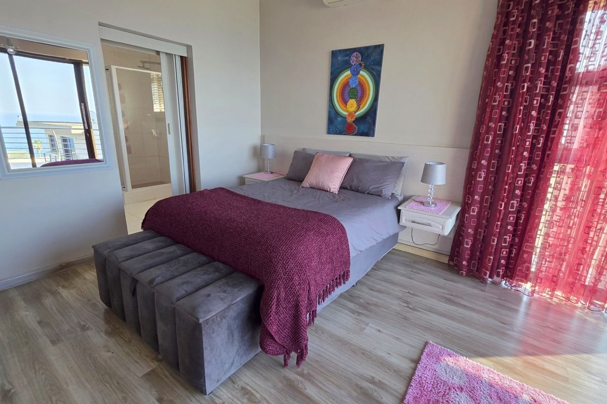 A well-lit bedroom featuring light wood-look flooring, a built-in headboard, and an en-suite bathroom with a glass-enclosed shower.