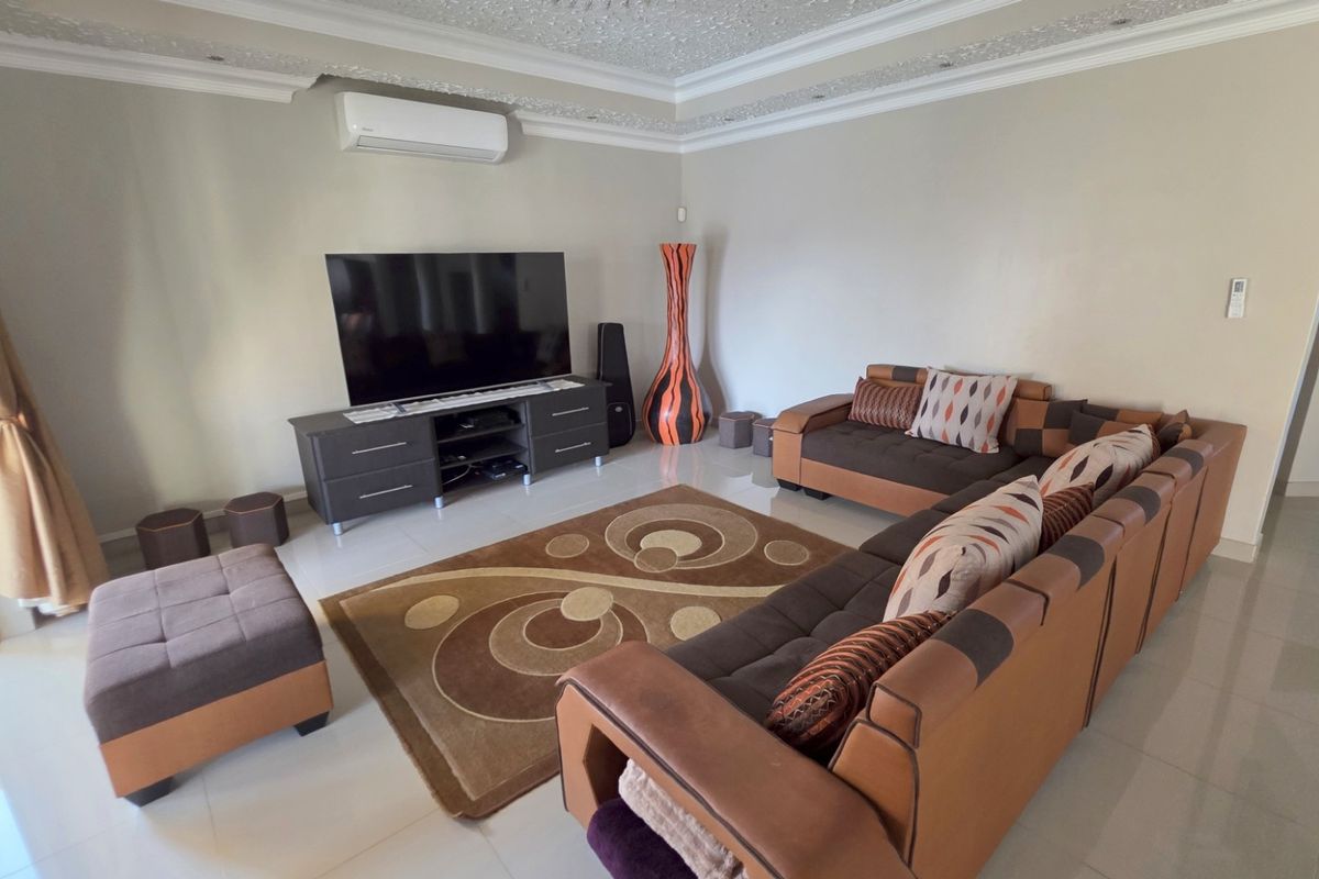 Spacious living room featuring tiled flooring, decorative ceiling cornicing, and a wall-mounted air conditioning unit.