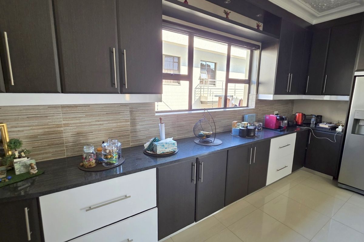 Modern kitchen featuring dark and white cabinetry, stone countertops, tiled backsplash, and large window providing natural light.