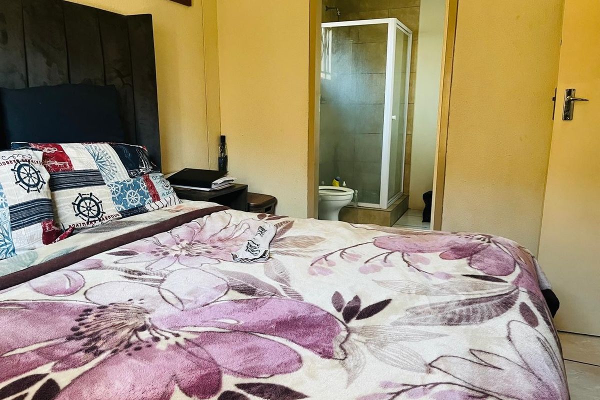 A bedroom featuring an en-suite bathroom with a glass-enclosed shower and tiled flooring.