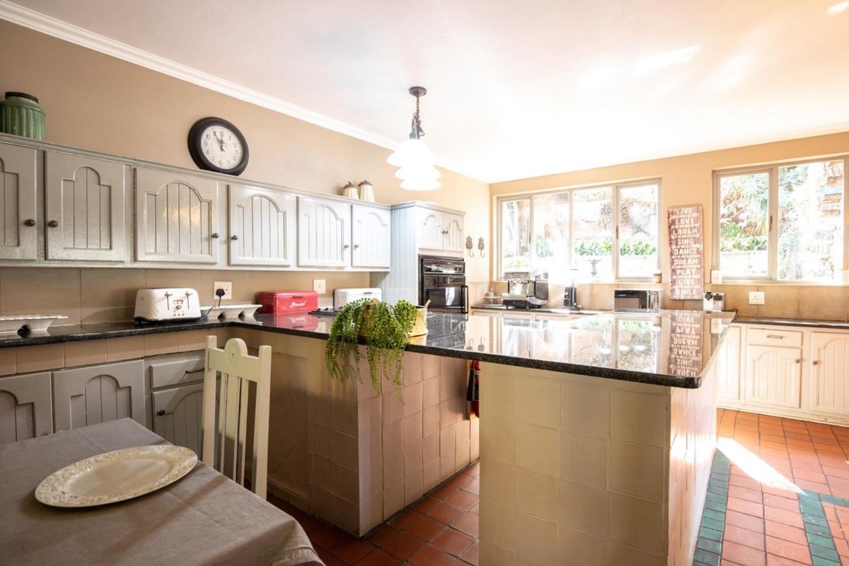 A spacious kitchen featuring granite countertops, a central tiled island, built-in oven, and terracotta flooring, offering a functional layout with ample natural light.
