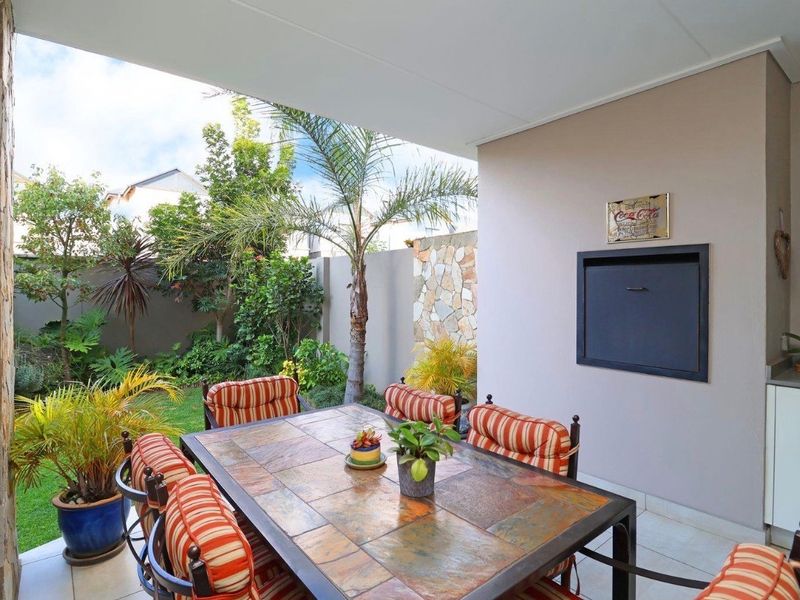 A covered patio area featuring a built-in braai, stone cladding accents, and tiled flooring, overlooking a private garden space.