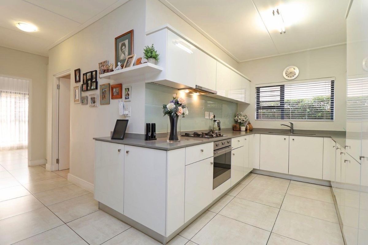 Modern kitchen featuring white high-gloss cabinetry, stone countertops, glass splashback, integrated oven, gas hob, and tiled flooring.
