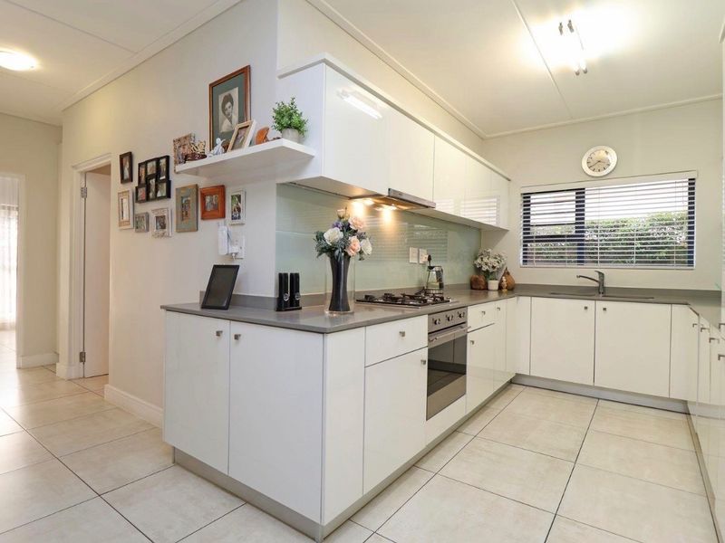 Modern kitchen featuring white high-gloss cabinetry, stone countertops, glass splashback, integrated oven, gas hob, and tiled flooring.