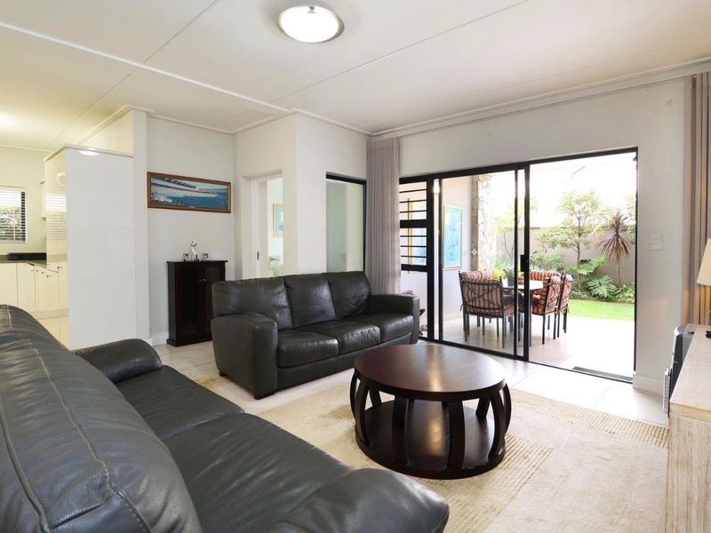 Open plan living area featuring tiled floors and sliding glass doors leading to a private patio and garden, with an adjacent kitchen space.