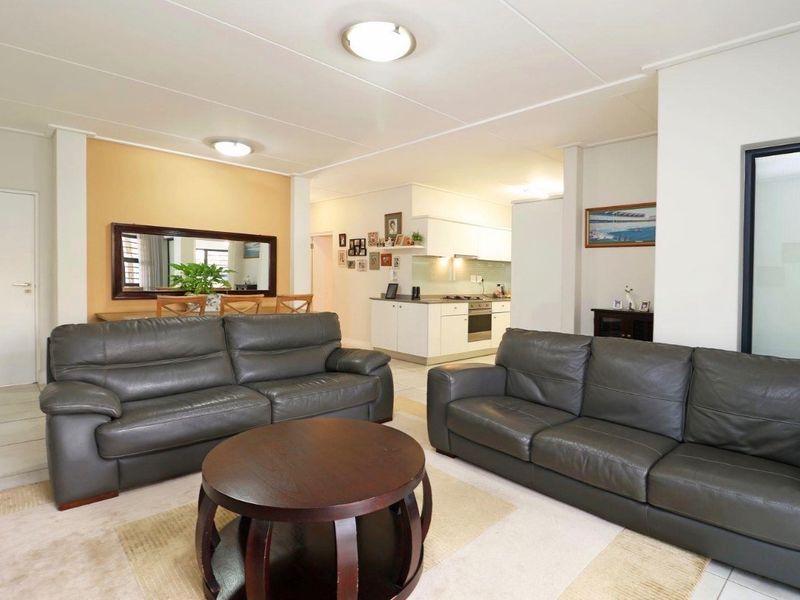 Open-plan living and dining area featuring a functional kitchen with built-in appliances and tiled flooring throughout.