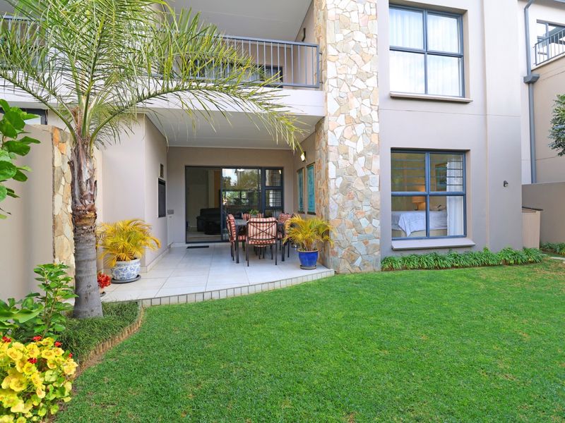 A well-maintained rear exterior view featuring a covered tiled patio, stone-clad pillar, and a private landscaped garden area.