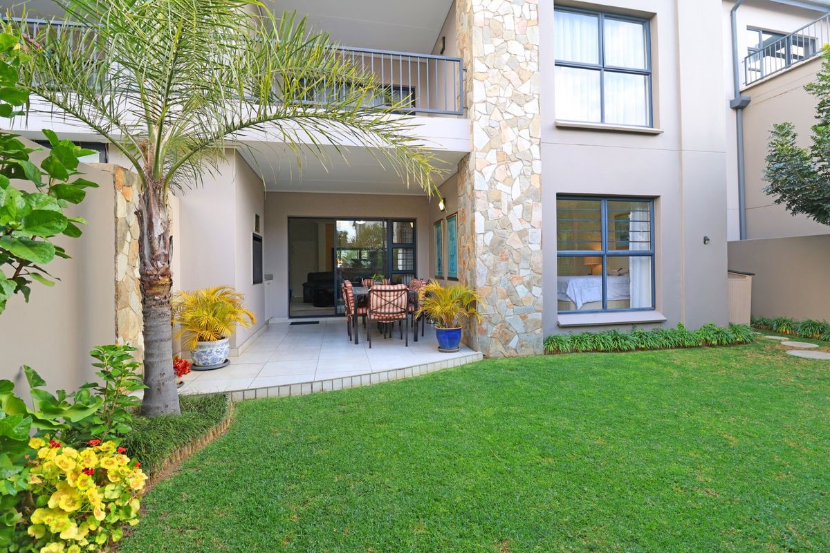 A well-maintained rear exterior view featuring a covered tiled patio, stone-clad pillar, and a private landscaped garden area.