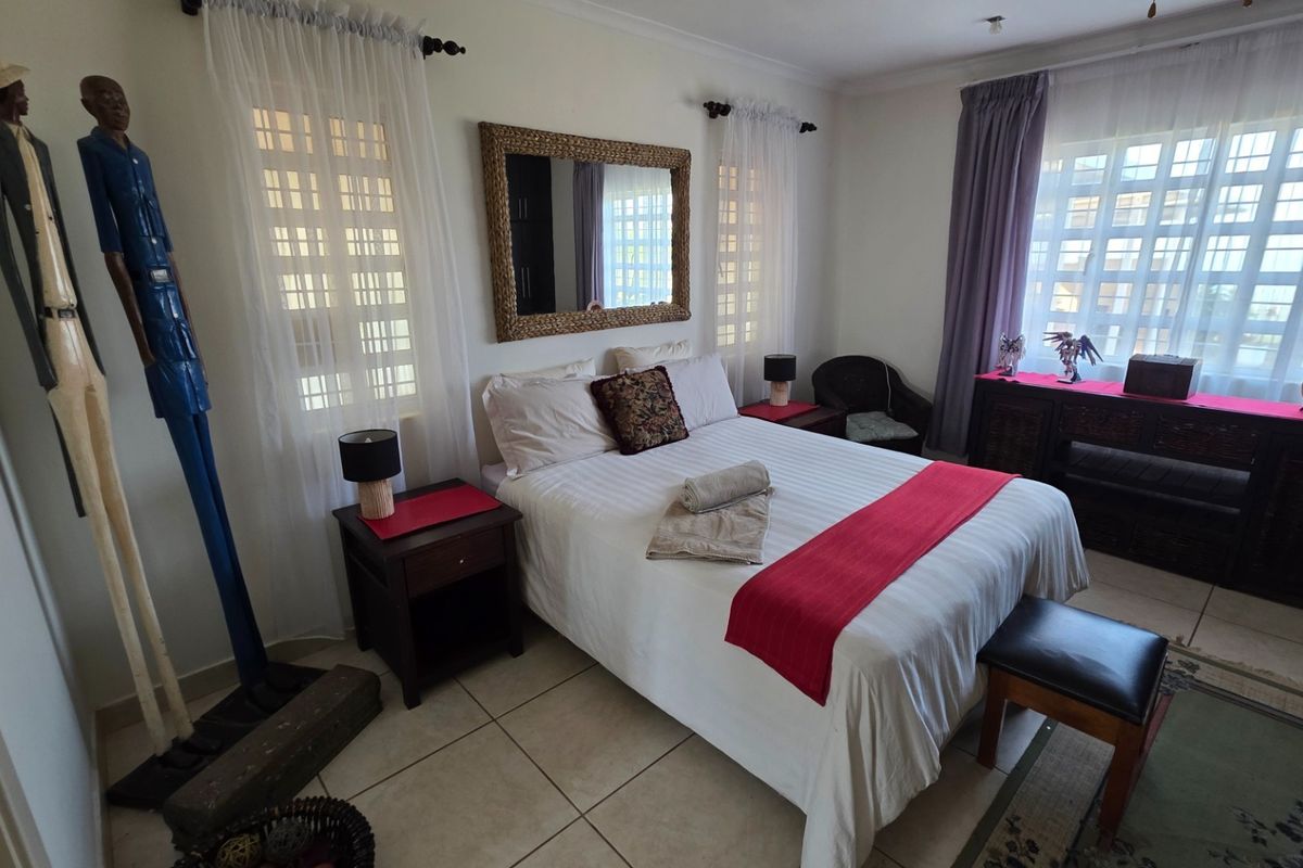 A well-lit bedroom featuring tiled flooring, large windows with security bars, and neutral wall finishes.