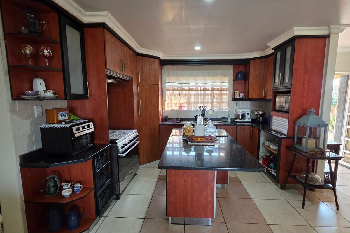 A functional kitchen featuring wood-tone cabinetry, a central island with granite countertops, a built-in oven, and tiled flooring with natural light.