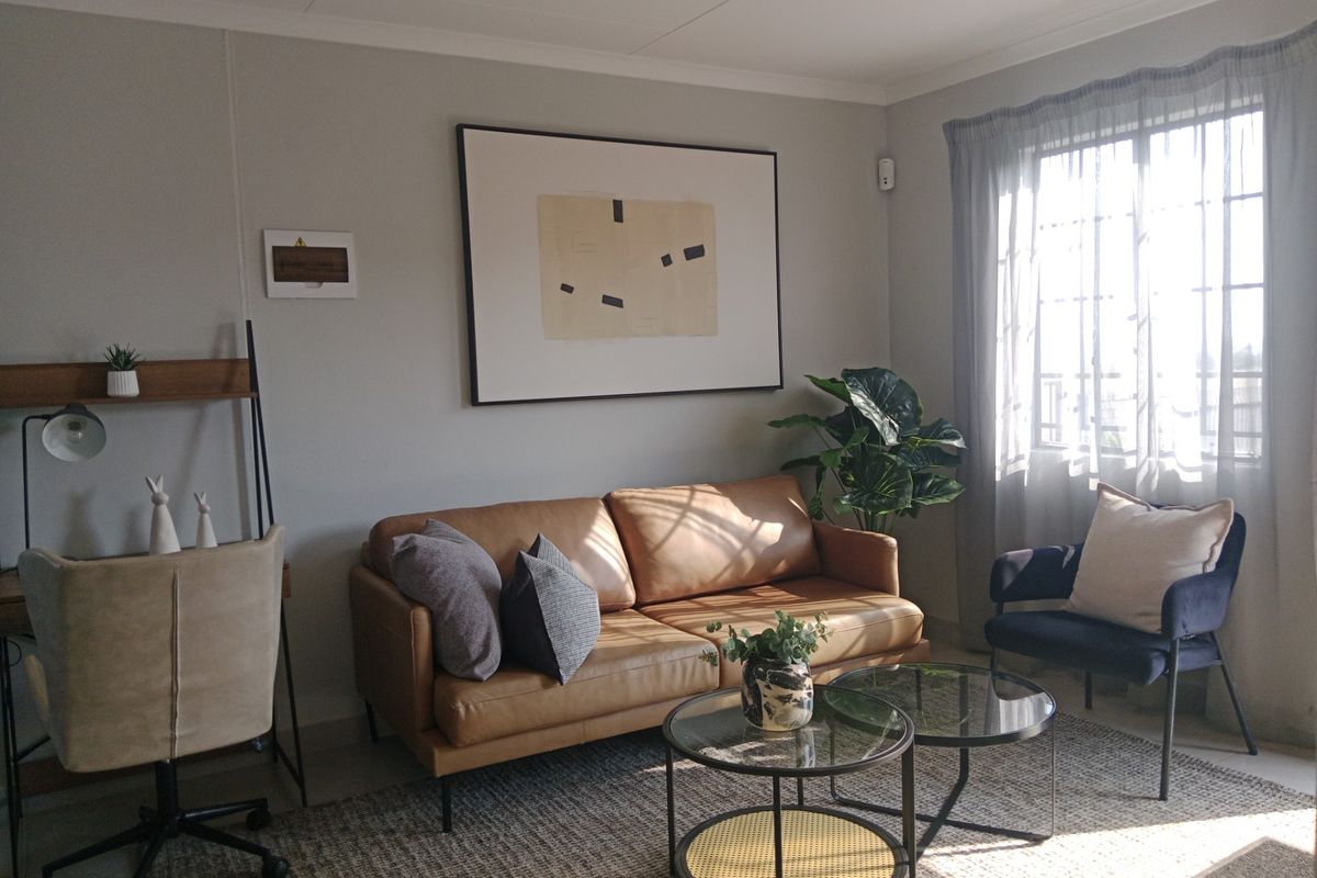 A well-lit living room featuring neutral wall tones, coved ceiling cornices, and a window with sheer curtains, creating a comfortable and inviting atmosphere.