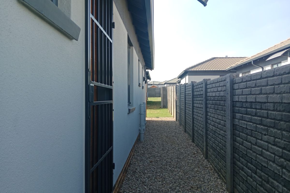 A side exterior walkway featuring a gravel path, security gate, and precast concrete boundary wall.