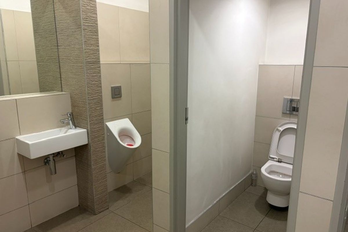 A clean, modern office bathroom featuring a wall-mounted basin, a wall-hung toilet, and a wall-mounted urinal with neutral tiled finishes.