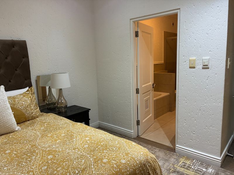 A bedroom featuring textured wall finishes and an en-suite bathroom with tiled flooring and a built-in bathtub.