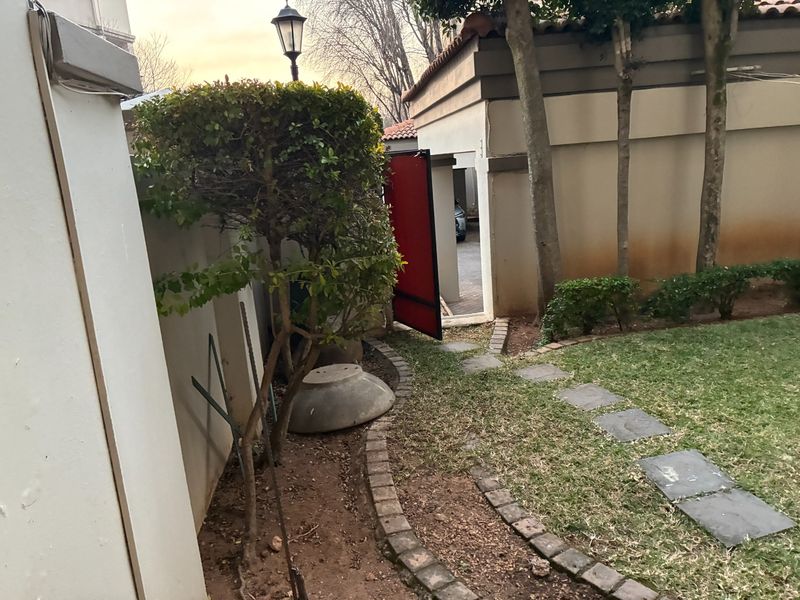A view of the side garden area featuring a paved walkway, boundary wall, and access gate leading to the driveway.