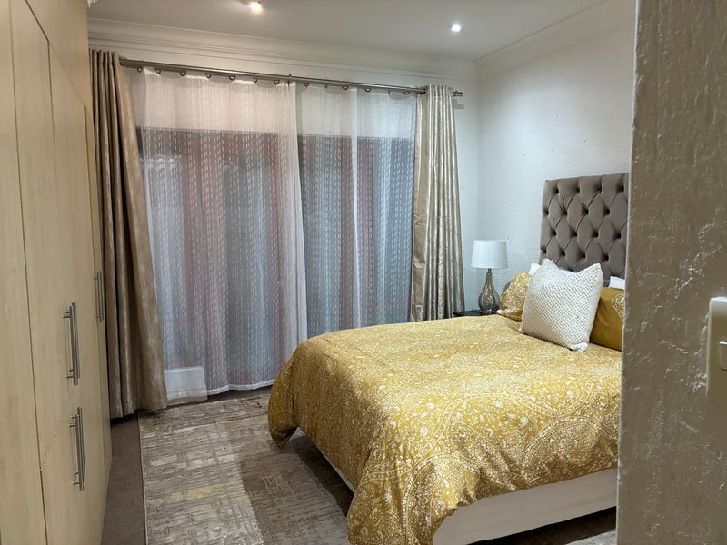 A well-maintained bedroom featuring built-in wooden cabinetry, recessed ceiling lighting, and large sliding glass doors with curtain tracks.