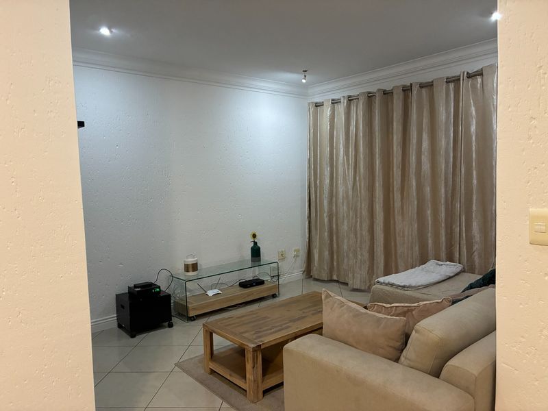 A comfortable living room featuring tiled flooring, recessed ceiling lighting, and floor-to-ceiling curtains.