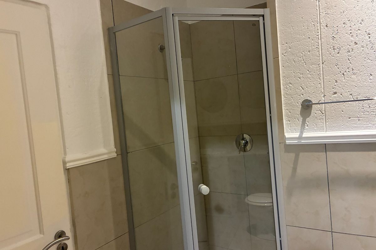 A functional bathroom featuring a corner shower enclosure with tiled walls and a towel rail.