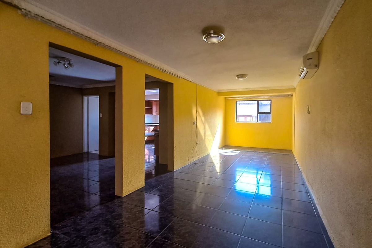 An open-plan living area featuring dark tiled flooring, yellow walls, and a wall-mounted air conditioning unit.