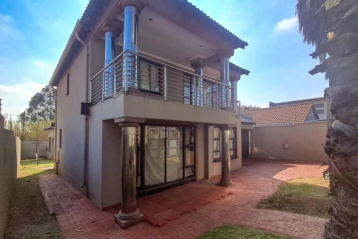 Rear view of the house featuring a covered patio on the ground floor and a balcony with stainless steel railings on the upper level.