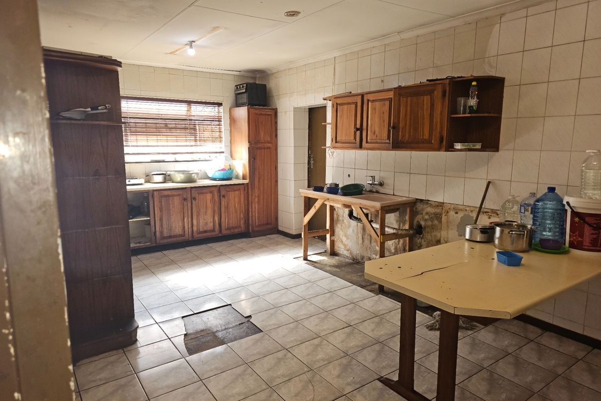 A dated kitchen featuring wooden cabinetry and tiled surfaces, currently requiring significant renovation and repair to the flooring and wall finishes.