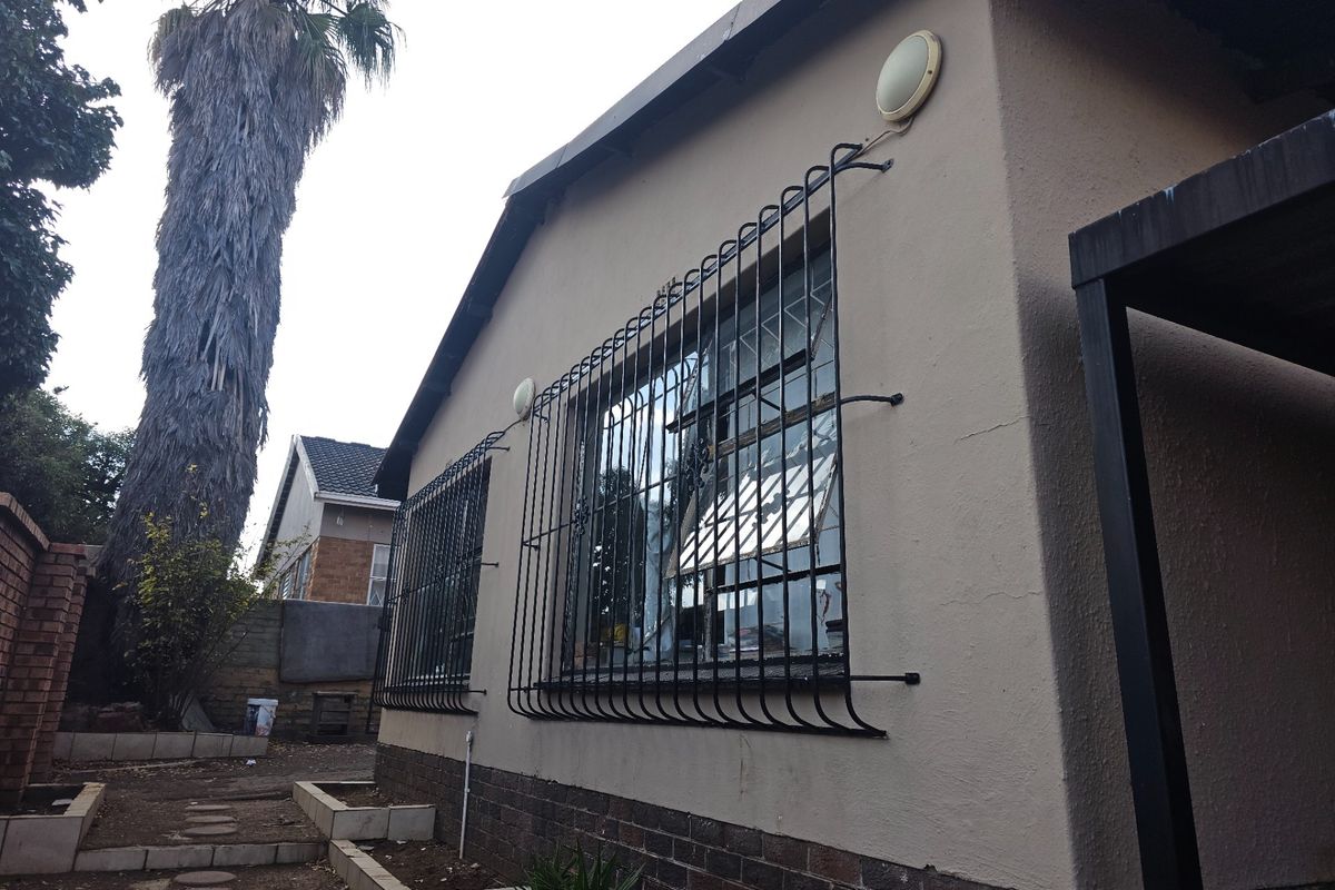 Rear exterior view of the property featuring security bars on windows, external wall lighting, and tiered garden beds.