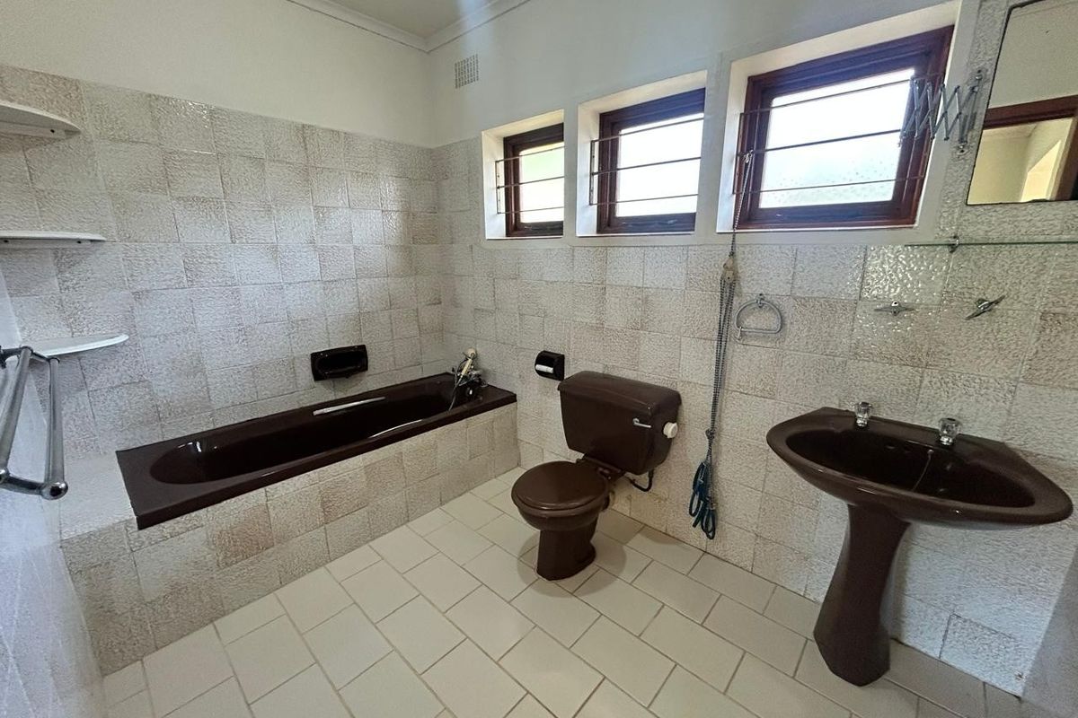 A dated bathroom featuring a brown bathtub, pedestal basin, and toilet with neutral wall and floor tiling.