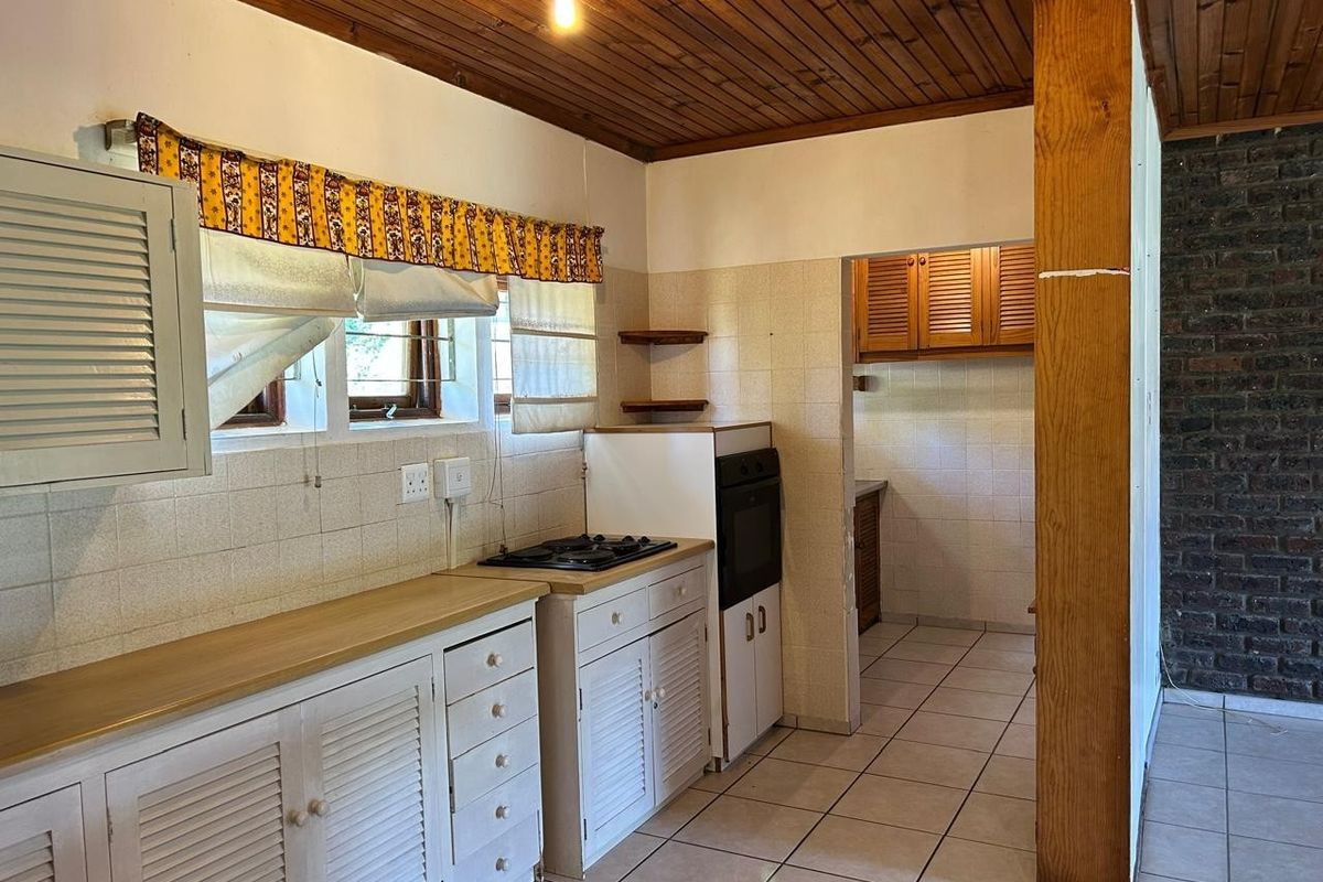 A dated kitchen featuring timber ceilings, tiled flooring, built-in cabinetry, and a separate scullery area with additional storage.