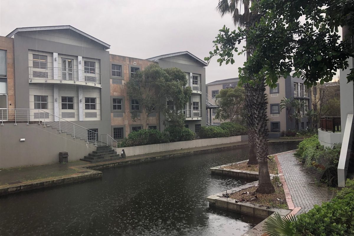 Exterior view of a multi-story office complex featuring modern facade design, balconies, and a landscaped canal-side walkway.