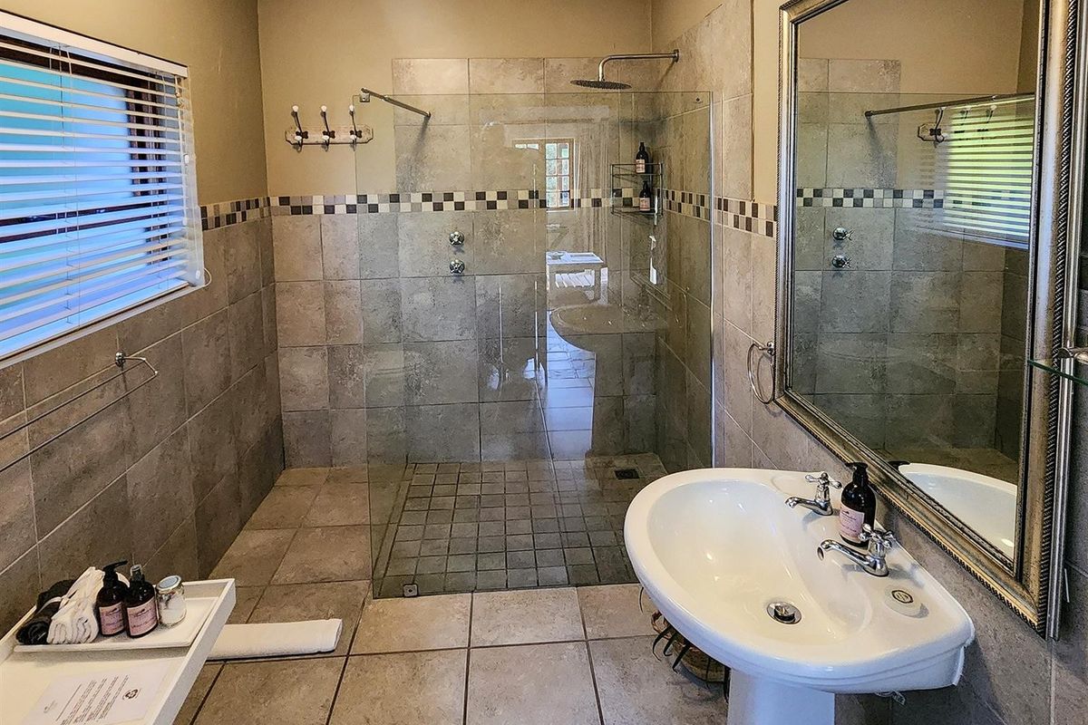 A well-maintained bathroom featuring a walk-in glass shower enclosure, pedestal basin, and neutral ceramic wall and floor tiling.