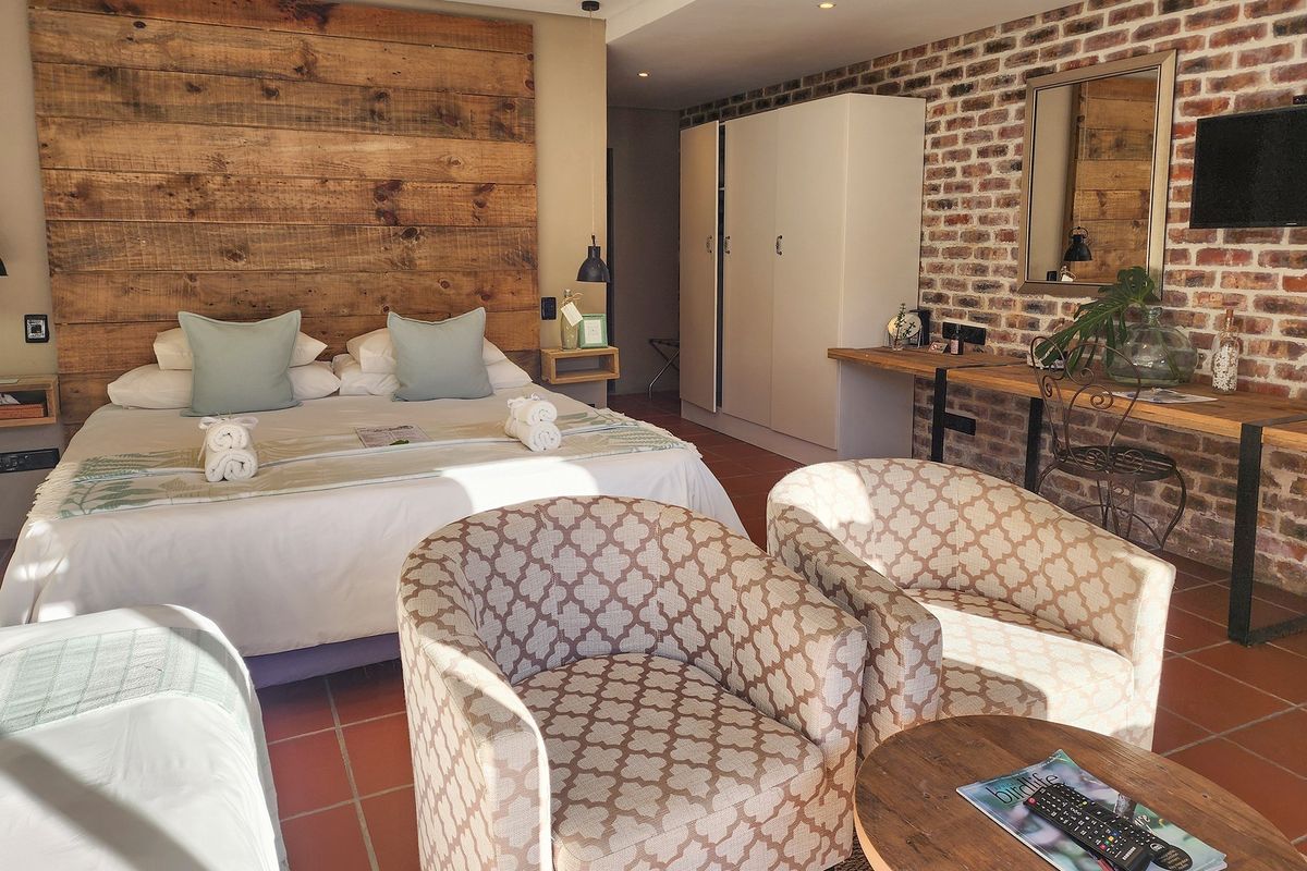 A well-appointed bedroom featuring a rustic timber headboard, exposed brick feature wall, terracotta floor tiles, and built-in wardrobe storage.
