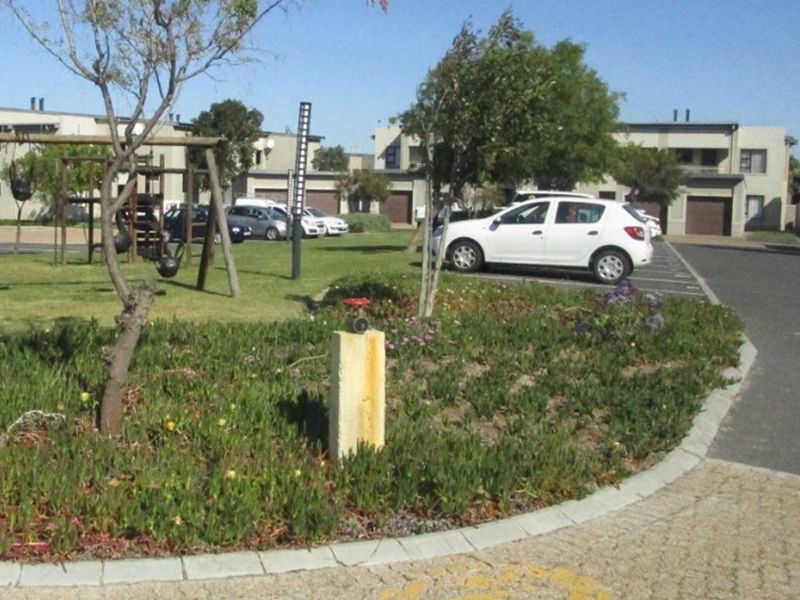 Exterior view of the apartment complex grounds featuring paved parking areas, landscaped garden spaces, and a communal children's play area.