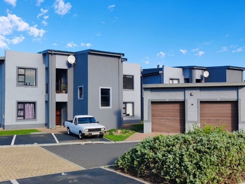 Front view of a modern apartment complex featuring grey painted brick facades, aluminium window frames, and a double garage with roller doors.