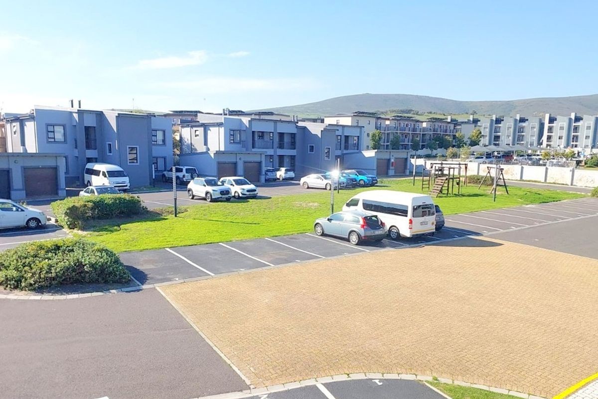 An elevated aerial view of the apartment complex grounds, featuring paved parking bays, communal green spaces, and a playground area.