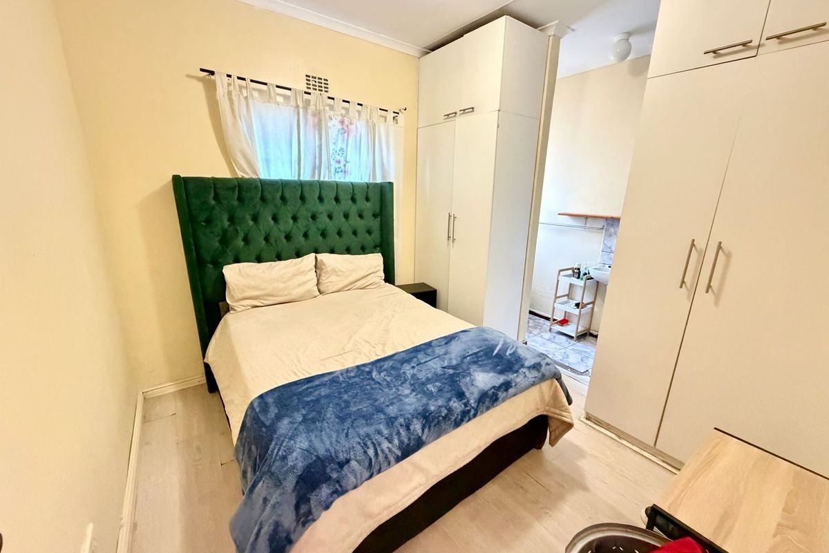 A bedroom featuring built-in cupboards and an adjoining en-suite bathroom area with light-toned flooring and neutral wall finishes.