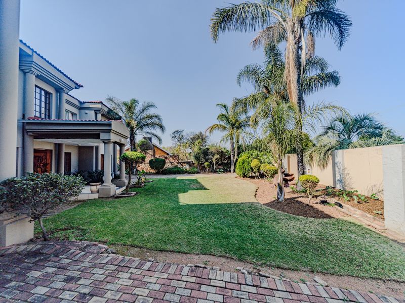 Spacious rear garden featuring a covered patio, well-maintained lawn, mature palm trees, and perimeter boundary walls.