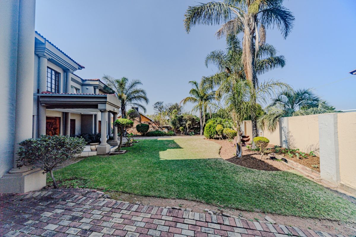 Spacious rear garden featuring a covered patio, well-maintained lawn, mature palm trees, and perimeter boundary walls.