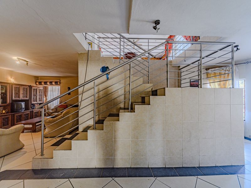 Open plan living area featuring a central tiled staircase with a modern stainless steel balustrade and ceramic floor tiling throughout.