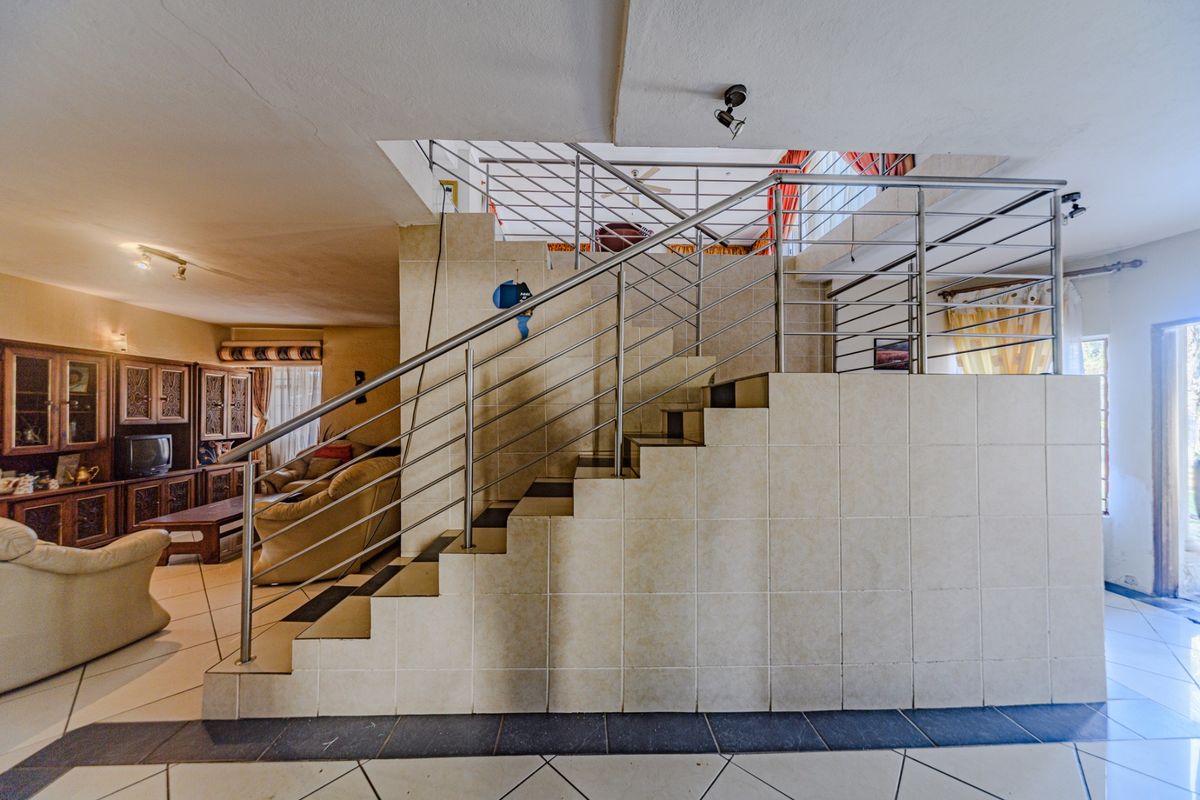 Open plan living area featuring a central tiled staircase with a modern stainless steel balustrade and ceramic floor tiling throughout.
