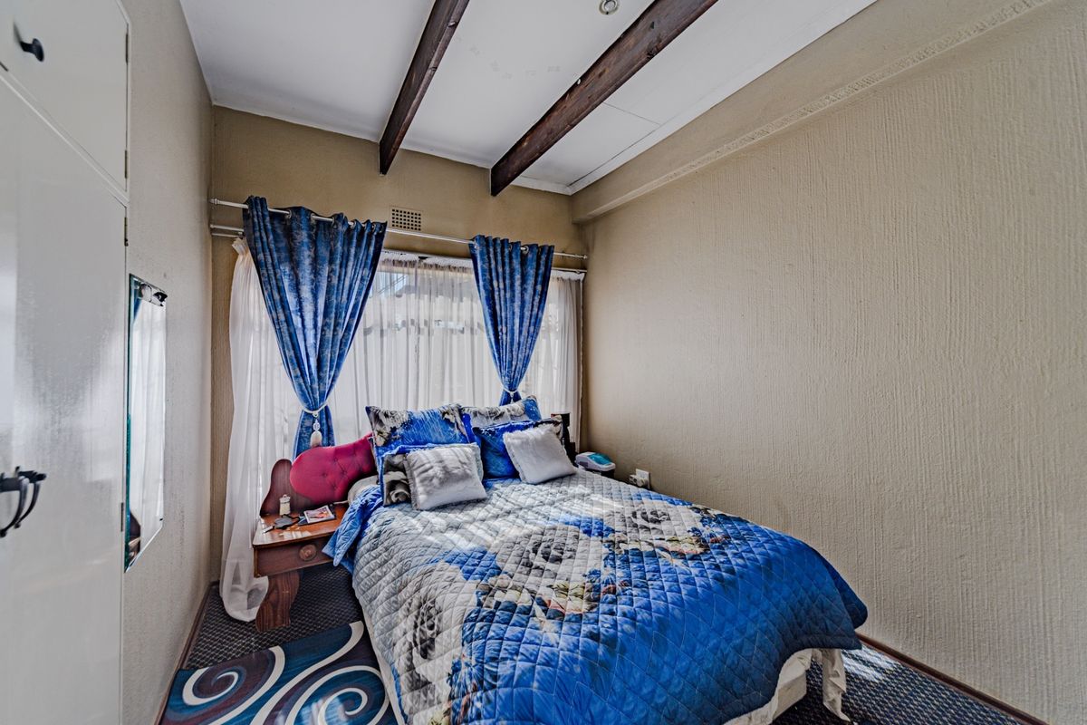 A cozy bedroom featuring exposed timber ceiling beams, textured walls, and a built-in cupboard, offering a functional space with potential for modern updates.