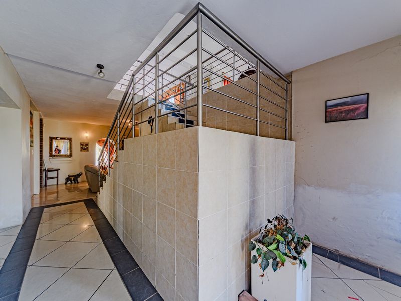 Hallway featuring a tiled staircase with a stainless steel balustrade and ceramic flooring, showing signs of wear on the adjacent wall.