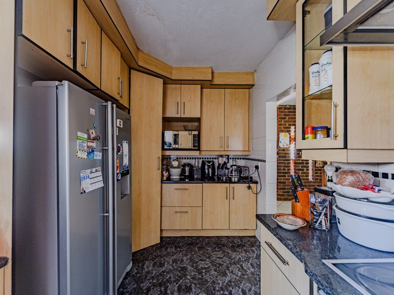 A functional kitchen featuring laminate cabinetry, granite countertops, and a tiled backsplash, showing signs of wear and ceiling water damage.