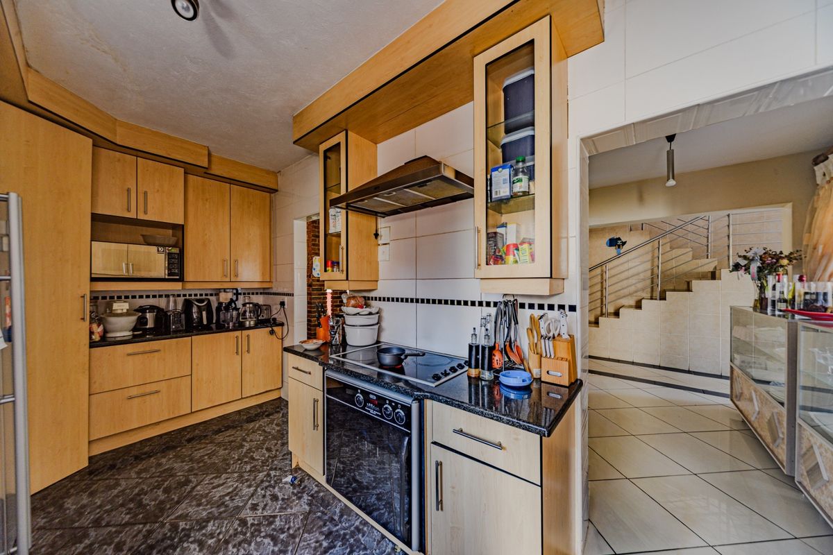 A functional kitchen featuring light wood cabinetry, granite countertops, built-in oven, and hob, with tiled flooring and a view towards the staircase.