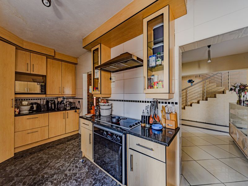 A functional kitchen featuring light wood cabinetry, granite countertops, built-in oven, and hob, with tiled flooring and a view towards the staircase.